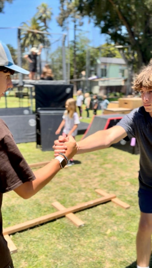 Two people shaking hands outdoors with a grassy area and trees in the background